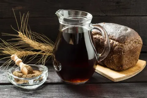 Dzbanek z ciemnym napojem, bochenek chleba, kłosy zboża i miseczka z mąką. Czy podpiwek ma alkohol? To pytanie nurtuje wielu.