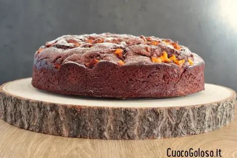 Torta al cioccolato con pezzi di mango, spolverata di zucchero a velo, su un tagliere di legno grezzo.