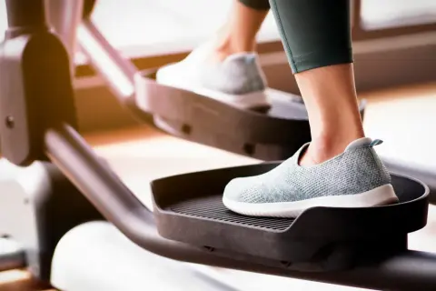 Kobieta ćwiczy na orbitreku, co jest świetnym sposobem na zapobieganie zanikowi mięśni nóg.