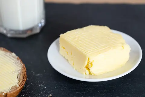 Frisch gemachte Butter auf einem Teller, daneben eine Scheibe Brot mit Butter bestrichen. So einfach kann Butter selber machen sein!