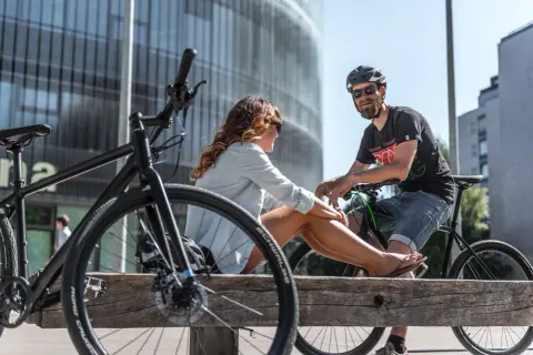 Ein Paar entspannt sich auf einer Holzbank mit Fahrrädern in einer modernen Stadt. Hier lebt es sich fahrradfreundlich.