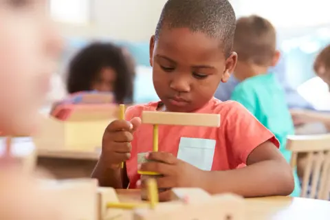 Ein Junge in einer Montessori-Schule baut konzentriert mit Holzbausteinen. So lernt man hier spielerisch.
