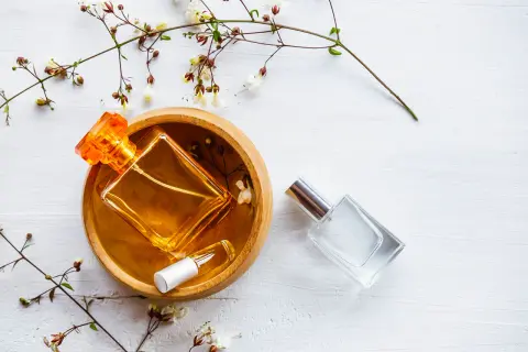 Dwie buteleczki perfum, jedna z bursztynowym płynem w drewnianej miseczce, druga szklana. Delikatne gałązki z kwiatami. Woda toaletowa ile alkoholu?