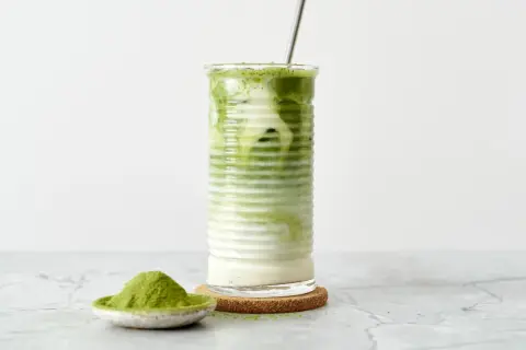 Un verre de matcha frappé, crémeux et rafraîchissant, avec une cuillère de poudre de matcha à côté.