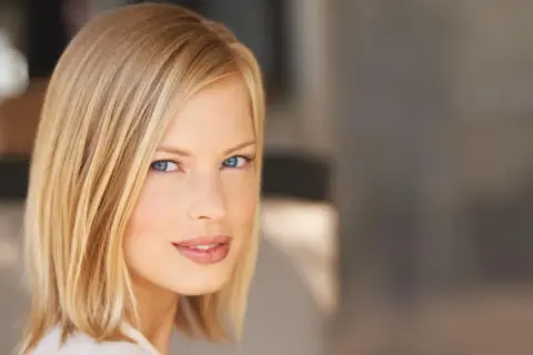 Kobieta z blond włosami w modnym clavi cut, z niebieskimi oczami i delikatnym uśmiechem.