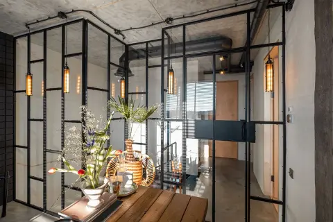 Interior moderno con paredes de cristal, lámparas colgantes y un arreglo floral sobre una mesa de madera.