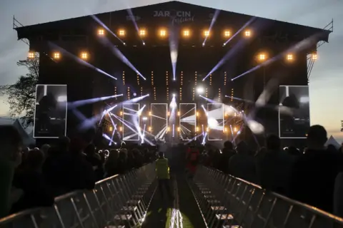 Jarocin Festival rozświetlony tysiącami świateł. Tłum czeka na koncert, a na scenie widać artystów.