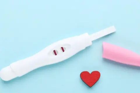 Pozytywny test ciążowy z dwoma czerwonymi kreskami. Kiedy zrobić test ciążowy? Serce symbolizuje miłość i nadzieję.