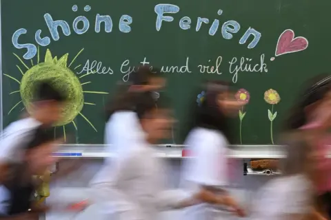 Schöne Ferien! Kinder eilen an einer Tafel vorbei, auf der Sonne, Blumen und ein Herz gemalt sind. Endlich sind die Sommerferien da!