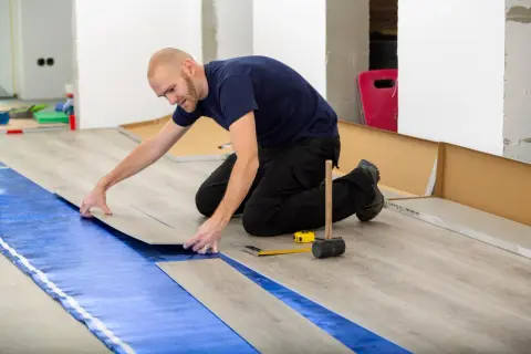 Pose d'un revêtement de sol stratifié sur une sous-couche bleue, assurant une isolation phonique sous carrelage. Outils de pose à proximité.