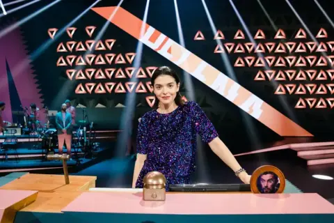 Eine Frau in Glitzerkleid steht im Rampenlicht, während eine Band im Hintergrund spielt. Wer stiehlt mir die Show?