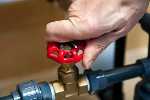 Dłoń obraca czerwony zawór grzybkowy, który jest częścią instalacji wodnej.