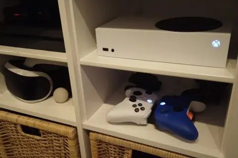 Biały Xbox Series S, który wyszedł w 2020 roku, stoi na półce obok konsoli PlayStation i kontrolerów.