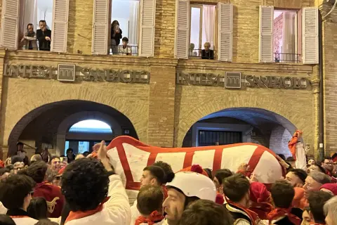 Folla festante al carnevale di Offida, con un grande carro bianco e rosso che avanza tra la gente.