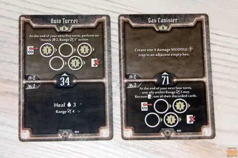 Dwie karty z gry planszowej Gloomhaven: "Auto Turret" i "Gas Canister", przedstawiające ikony akcji i statystyki postaci.