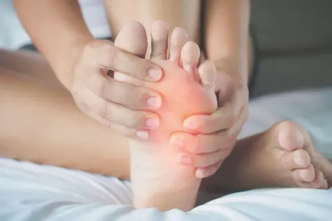 Mani che massaggiano la pianta del piede, evidenziando un'area arrossata che simboleggia il dolore.