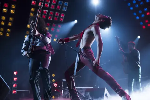 Freddie Mercury w czerwonym stroju, śpiewający na scenie, podczas gdy gitarzysta gra. To jest ich queen rhapsody.