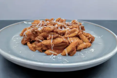 Gnocchi Sardi (Malloreddus) mit Tomatensoße und geriebenem Parmesan auf einem Teller.