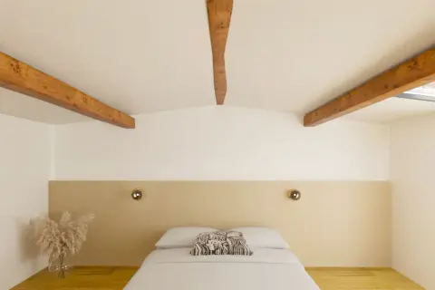 Chambre mansardée avec poutres apparentes. Quel mur peindre pour un effet cosy ? Le mur derrière le lit, avec sa tête de lit beige, semble idéal.