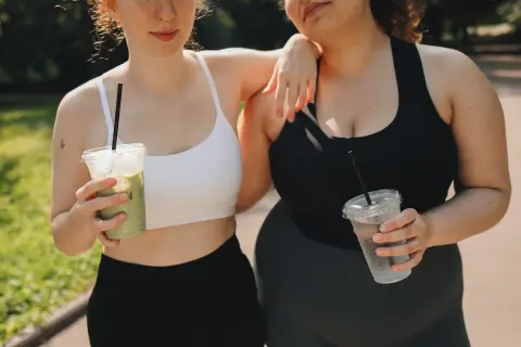 Due amiche con fianchi a violino si godono una bevanda fresca dopo l'allenamento, una con un matcha, l'altra con acqua.