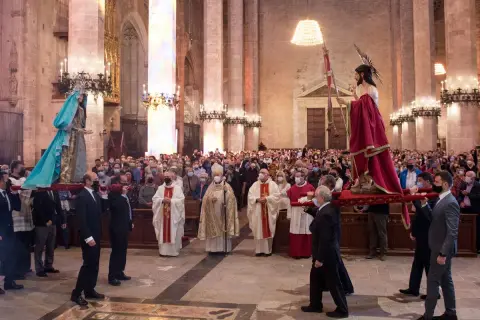 Procesión del Domingo de Resurrección en una catedral. Hombres portan imágenes religiosas mientras fieles observan.
