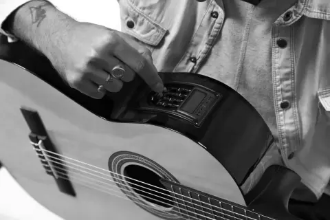 Dłoń z pierścionkami reguluje pokrętła na gitarze klasycznej. Nuty czekają na wykonanie.
