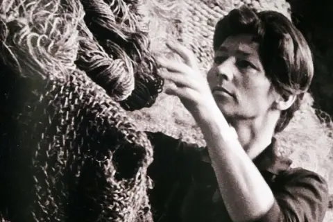 Magdalena Abakanowicz dotyka swojej monumentalnej rzeźby z włókien, tworząc dzieło sztuki.