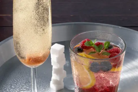 Ein prickelnder Champagner-Cocktail mit Beeren und Zitrone, daneben ein Glas mit sprudelndem Champagner und Zuckerspiralen.