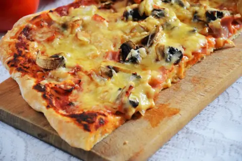 Pyszna pizza capriciosa z pieczarkami i szynką, roztopionym serem, na drewnianej desce.
