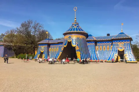 Blå och gul tältliknande byggnad med folk som sitter vid bord utanför i haga parken.