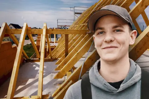 Junger Mann im Kapuzenpullover vor Dachstuhl. Informiert sich über zimmerer ausbildung gehalt netto.