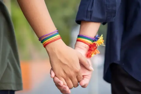 Dwie osoby trzymają się za ręce, nosząc tęczowe bransoletki. To symbol sprzeciwu wobec terapii konwersyjnej.