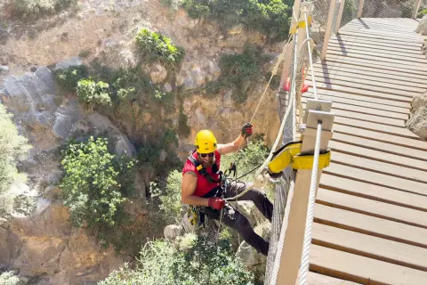Man i gul hjälm klättrar på en hängbro längs Caminito del Rey, en dramatisk klippstig.