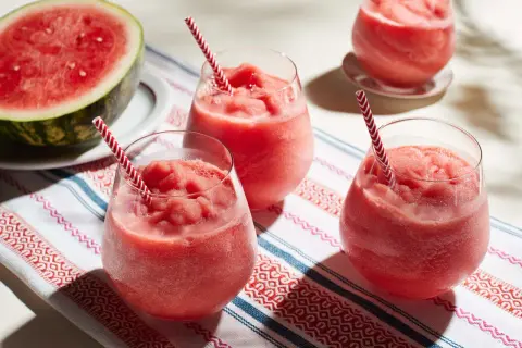 Fryst sallad med vattenmelon i glas med randiga sugrör. En halv vattenmelon ligger bredvid.