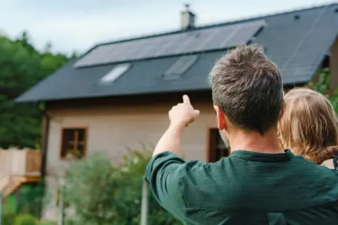 Hombre señala las placas solares virtuales en el tejado de una casa, mientras abraza a una niña.