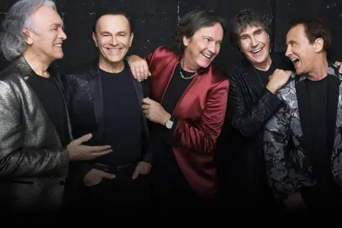 Cinque uomini sorridono, uno con giacca rossa, ricordando i testi di Renato Zero "Qualcuno mi renda l'anima".