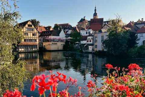 Blick auf Bamberg mit Fachwerkhäusern am Fluss. Rote Geranien im Vordergrund. Entdecken Sie Bamberg Geheimtipps!
