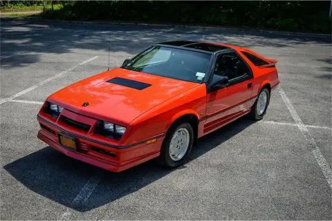 Pomarańczowy Dodge Daytona z czarnym dachem i spojlerem na parkingu.