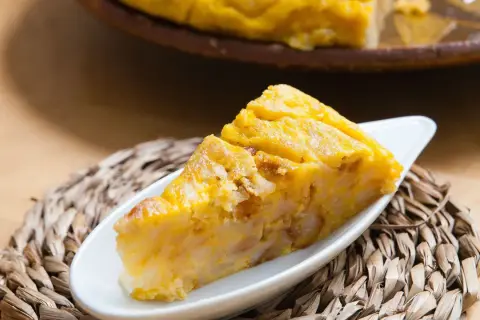 Una porción de tarta de choclo, dorada y apetitosa, servida en un plato blanco sobre una esterilla tejida.