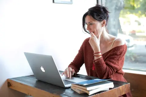 Kobieta przy laptopie, zamyślona, jakby udawała kogoś innego, by zdobyć nowe informacje.