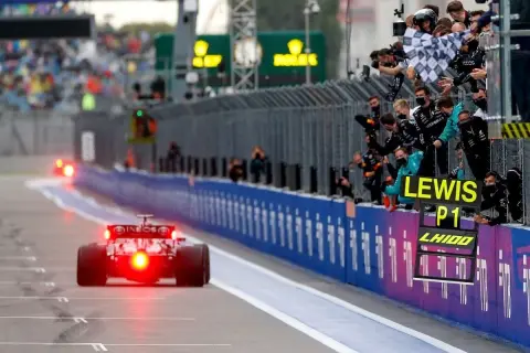 Un coche de Fórmula 1 cruza la meta, con el equipo celebrando la victoria de Lewis Hamilton en el gran premio.