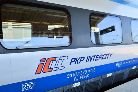 Boczna ściana pociągu PKP Intercity z logo IC. Widoczne okna, w których odbija się niebo i peron. To właśnie eic co to za pociąg!