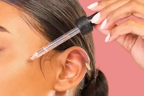 Dłoń z pipetką aplikuje serum na twarz. Odkryj metodę kanapkową efekty dla promiennej skóry.