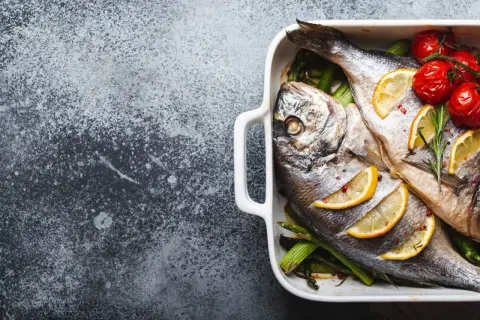 Deux poissons le saint pierre, cuits au four avec des citrons, des tomates cerises et des asperges dans un plat blanc.