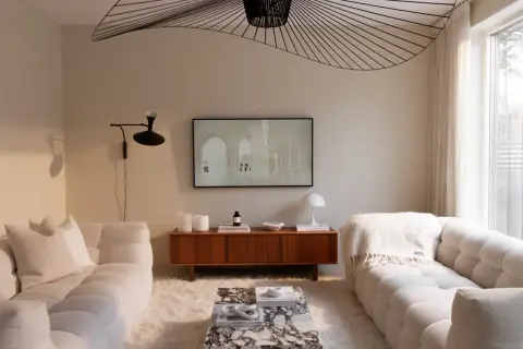 Ett vardagsrum i kall beige ton. Mjuka soffor, en marmorbänk och en träbyrå skapar en lugn atmosfär. En stor taklampa ger ett dramatiskt intryck.