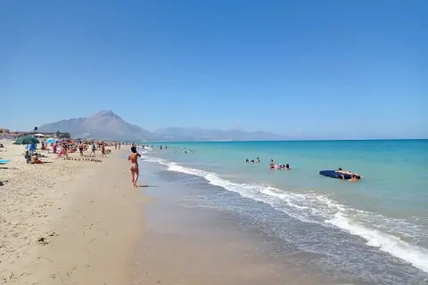 En solig stranddag vid Campofelice di Roccella med folk som badar och kopplar av.
