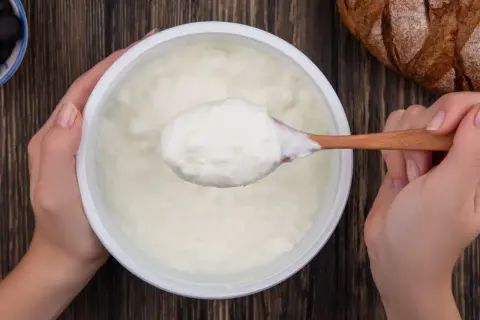 Gęsty, biały jogurt na drewnianej łyżce. To właśnie skyr, islandzki przysmak, który świetnie smakuje z chlebem i oliwkami.