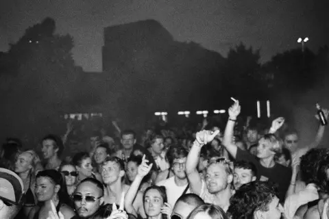 Folla in delirio a un concerto, con mani alzate e luci soffuse. Marco festa dj fa ballare tutti.