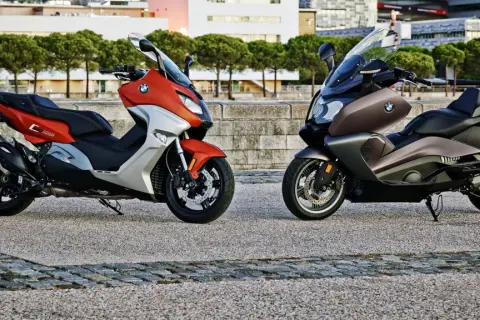 Dwa skutery BMW C650GT: jeden pomarańczowo-srebrny, drugi brązowy, stojące na kamiennym placu.