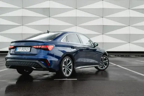Eleganckie, nowe Audi A3 w kolorze granatowym prezentuje się stylowo na tle nowoczesnej architektury.